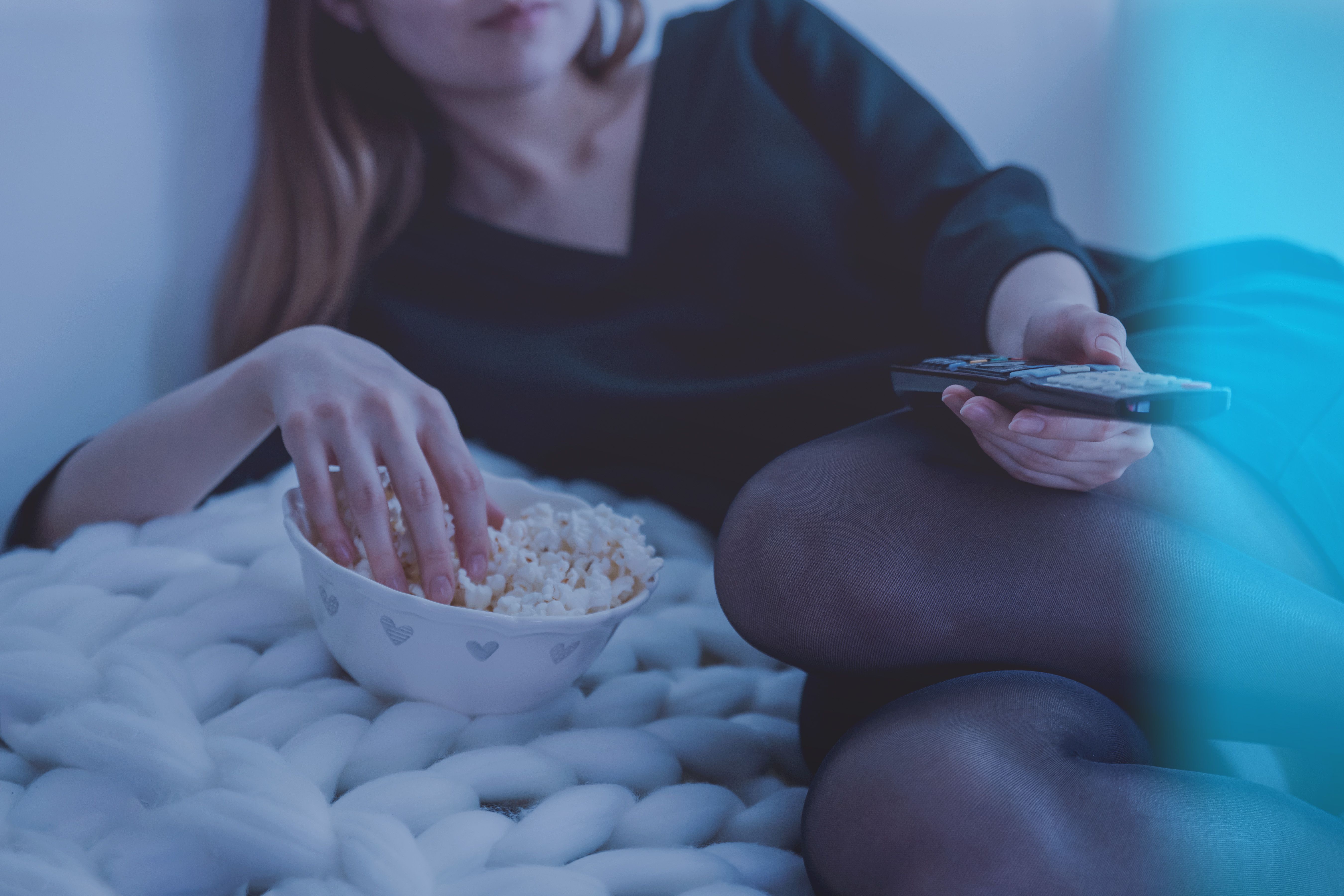 Cozy evening scene with woman enjoying popcorn and watching TV.