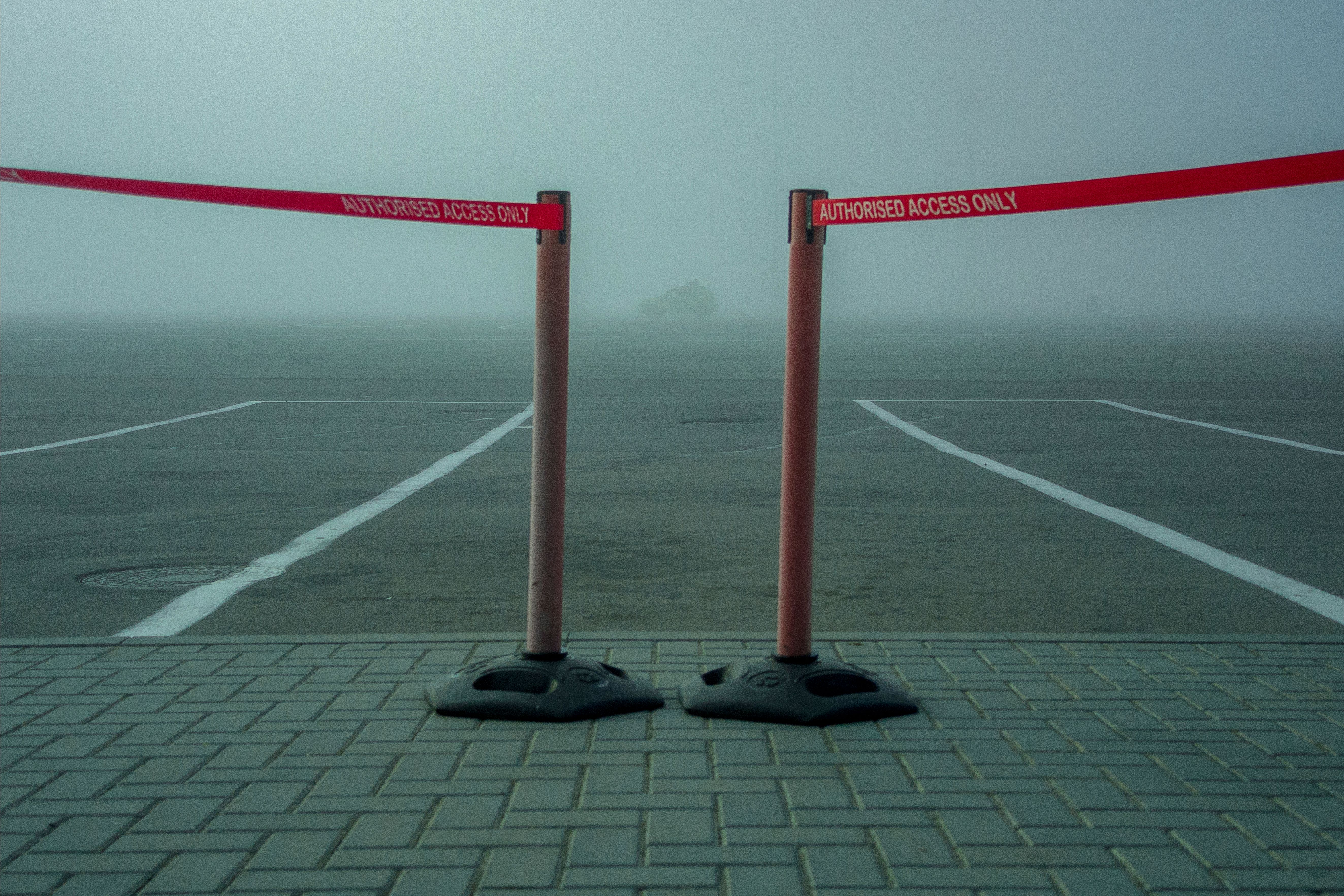 A foggy parking lot featuring a retractable barrier tape labeled 'AUTHORIZED ACCESS ONLY.'