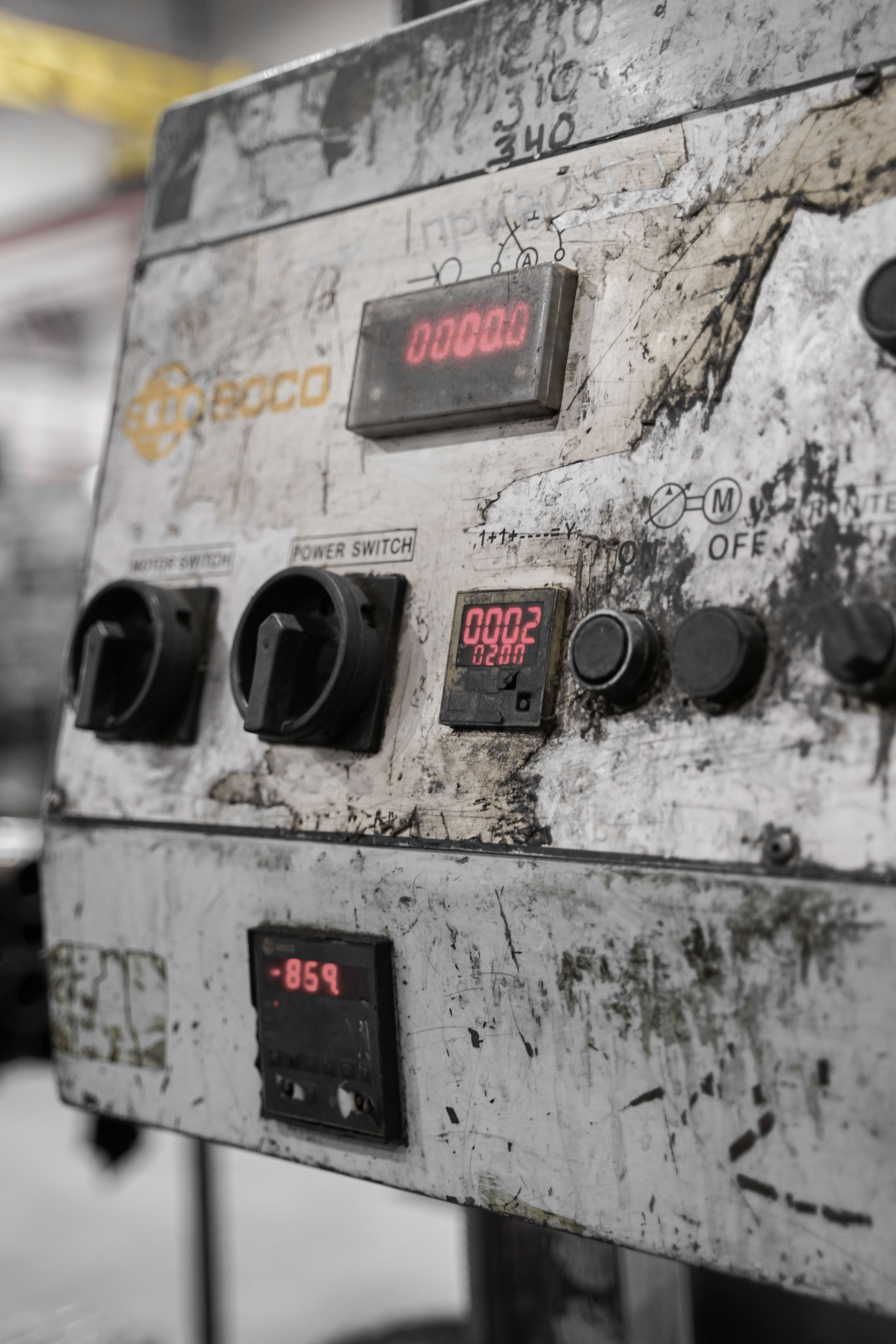 Close-up of a dirty and worn industrial machinery control panel with knobs and digital displays.