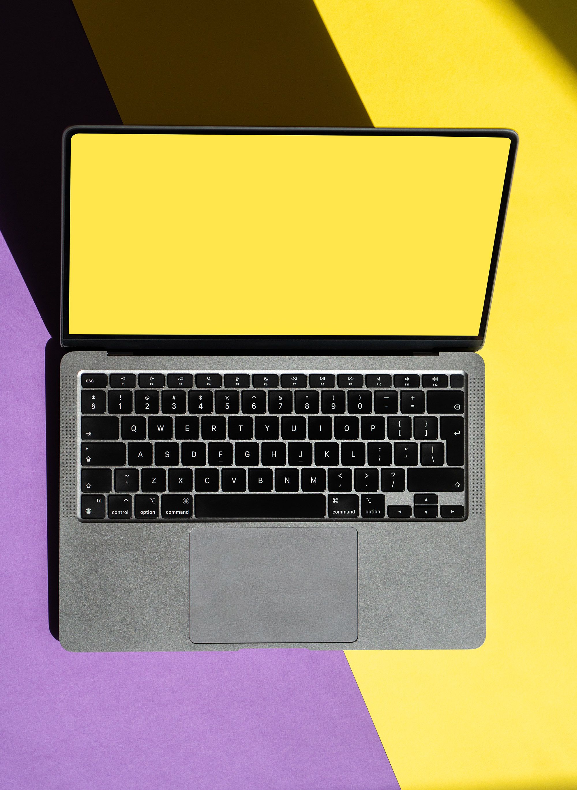 Top view of a laptop with a yellow screen on a vibrant yellow and purple backdrop.