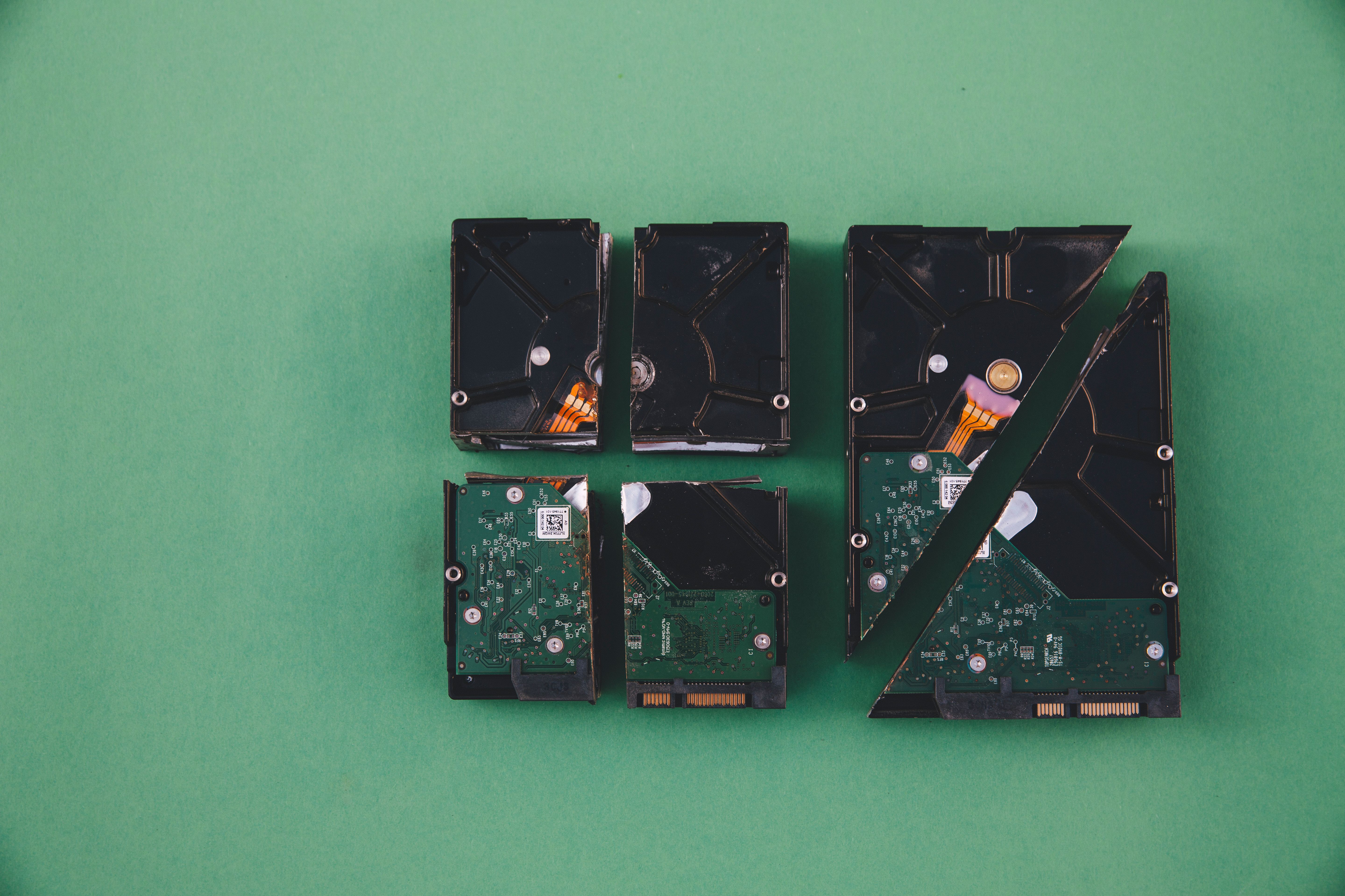 Four broken hard drives arranged on a green background, showcasing data destruction.