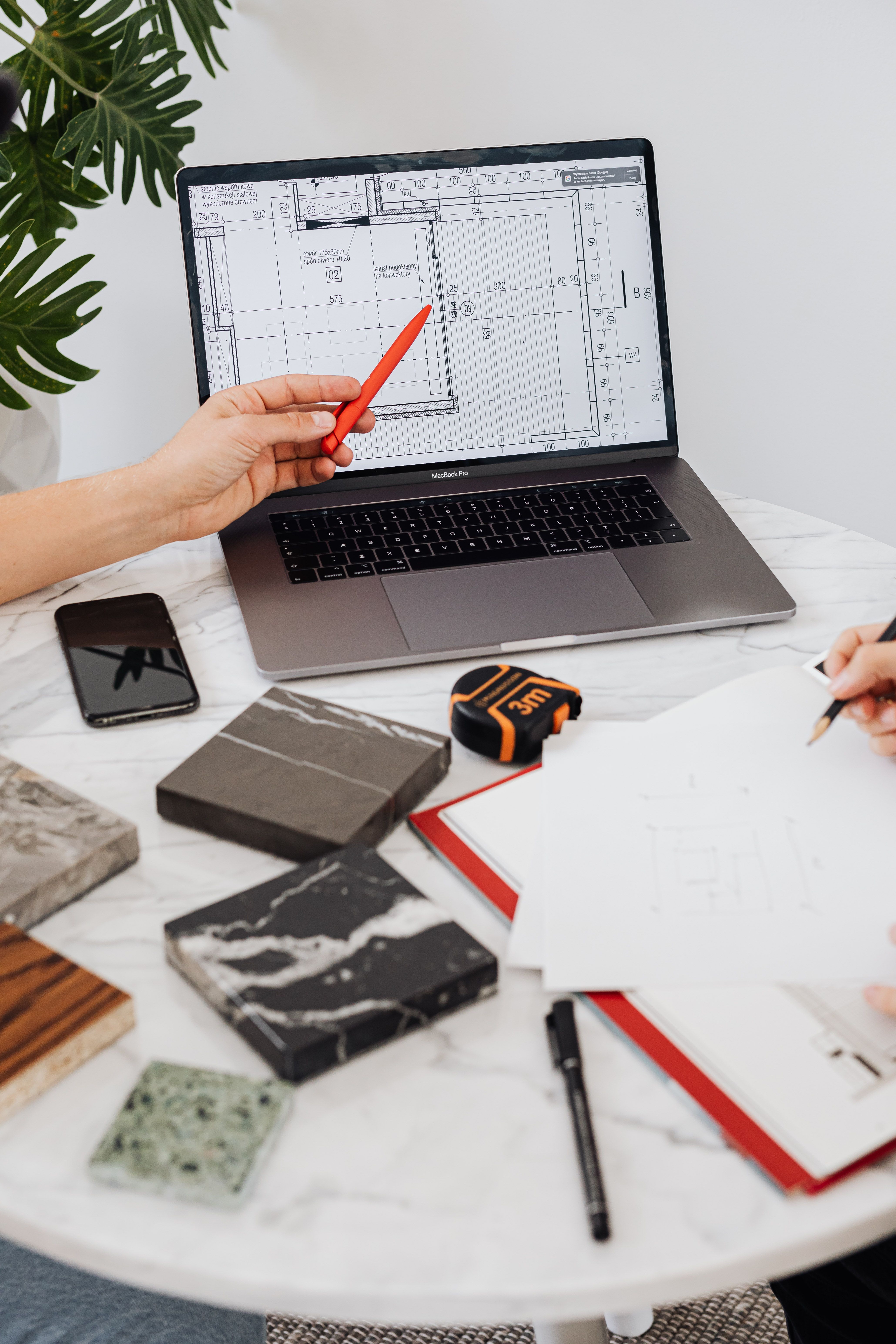 Interior designers reviewing tile samples and floor plans using a laptop and pen on a marble table.