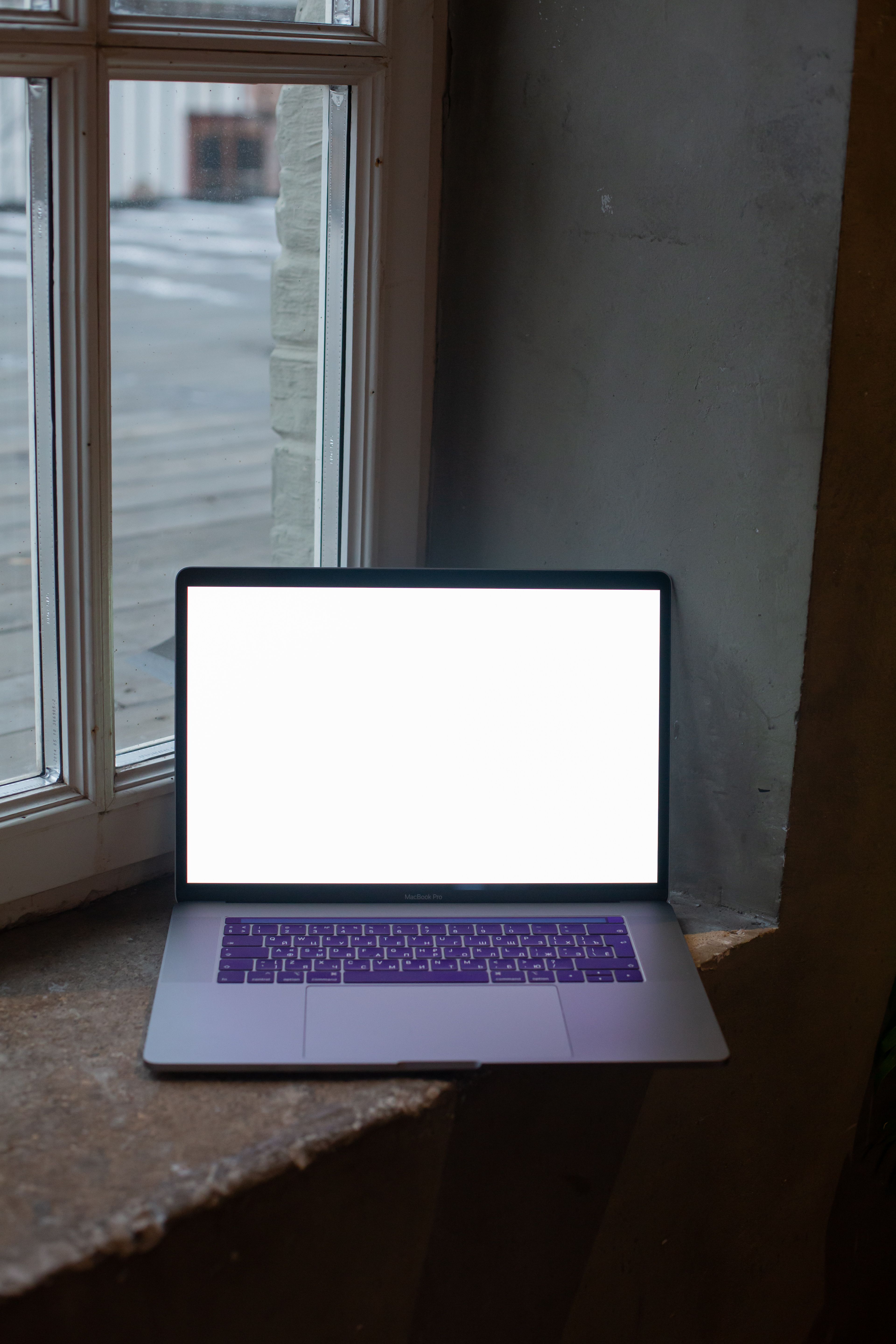 A laptop with a white screen placed on a window sill indoors.